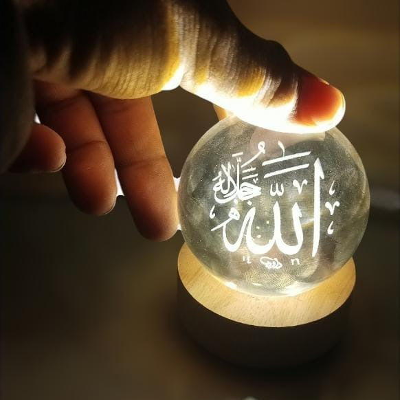 Hand holding a glowing crystal ball with engraved text on a wooden base.