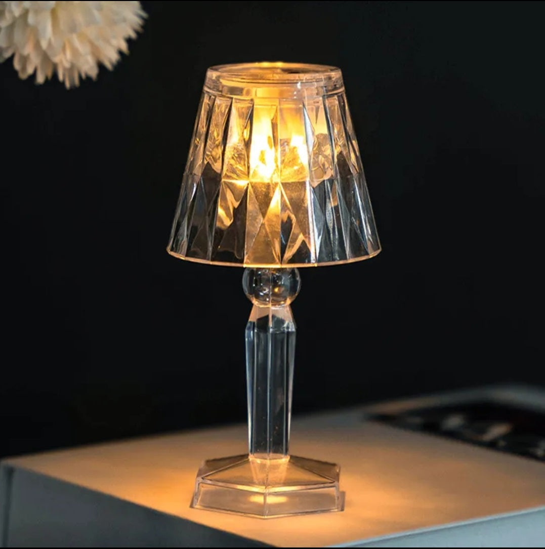 Small glass table lamp with a warm glow on a dark background