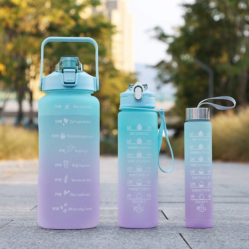Three gradient blue and purple water bottles with measurement markings outdoors.