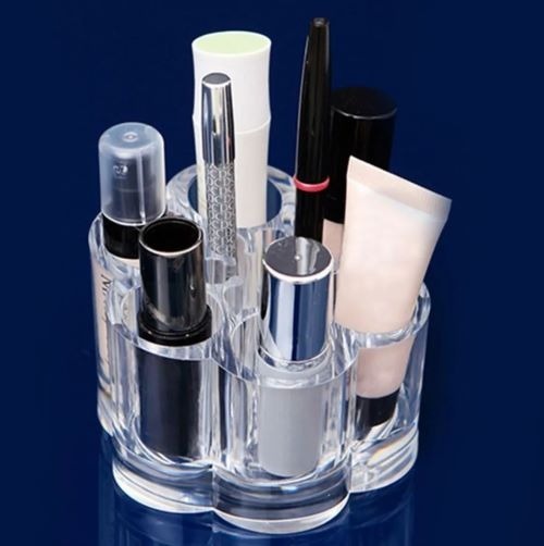 Clear acrylic cosmetic organizer with various makeup items on a dark blue background