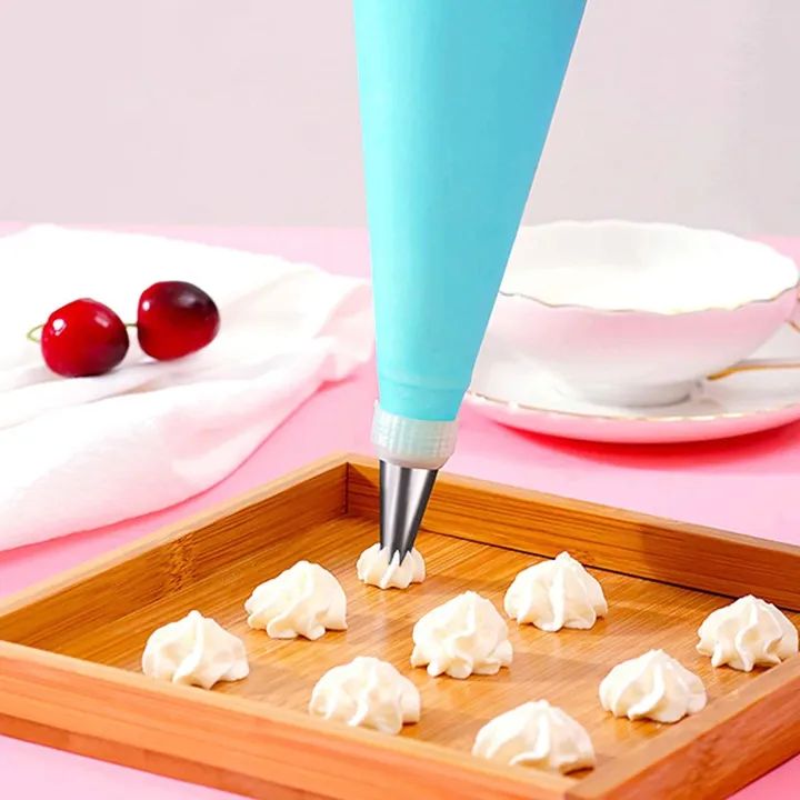 Baking tool with cream dollops on a wooden tray, cherry and tea set in the background.