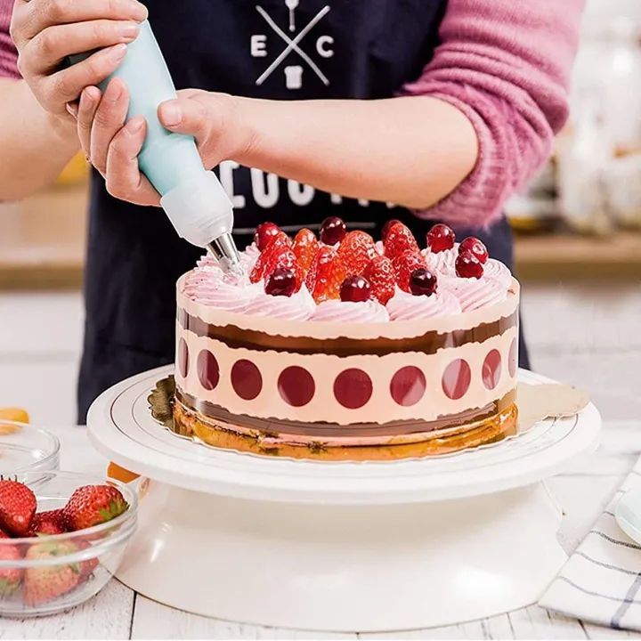 Person decorating a cake with strawberries using a piping bag in a kitchen setting.