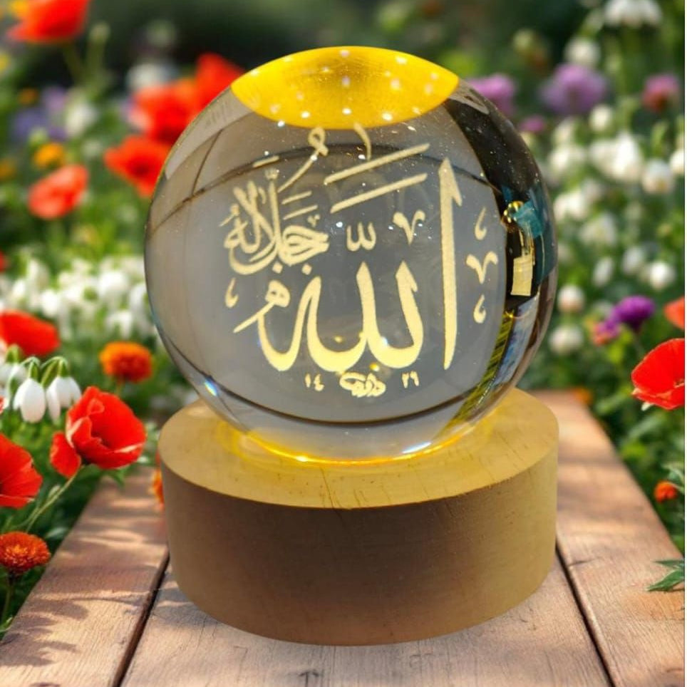 Decorative glass sphere with Arabic text on a wooden base, surrounded by flowers.