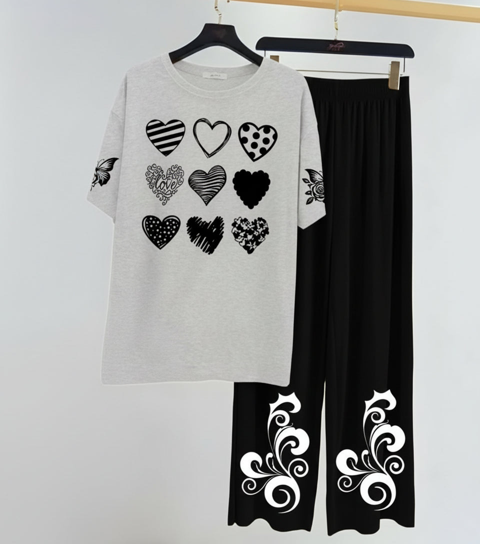 Gray sweatshirt with heart patterns and black pants with white designs on a hanger against a white background.